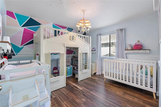 bedroom with a notable chandelier, dark wood-type flooring, and a nursery area