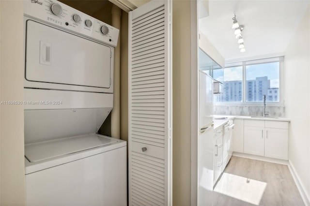 clothes washing area featuring track lighting, sink, stacked washer / dryer, and light hardwood / wood-style flooring