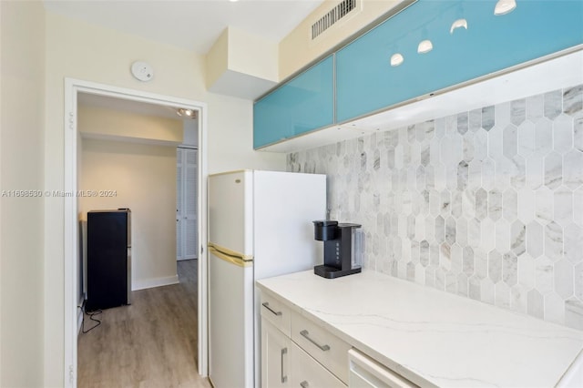 kitchen with white refrigerator, light stone countertops, and light hardwood / wood-style flooring