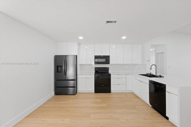 kitchen with light wood-type flooring, backsplash, sink, black appliances, and white cabinets