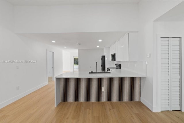 kitchen with kitchen peninsula, sink, light hardwood / wood-style flooring, appliances with stainless steel finishes, and white cabinetry