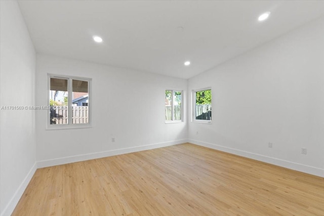 empty room featuring light wood-type flooring, vaulted ceiling, and a healthy amount of sunlight