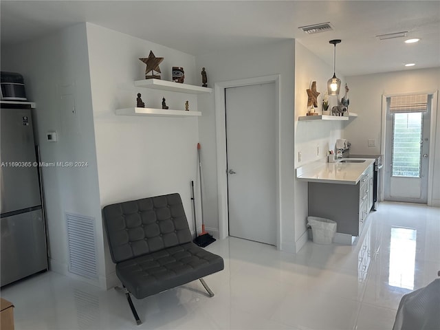 interior space with pendant lighting, light tile patterned floors, stainless steel refrigerator, and sink