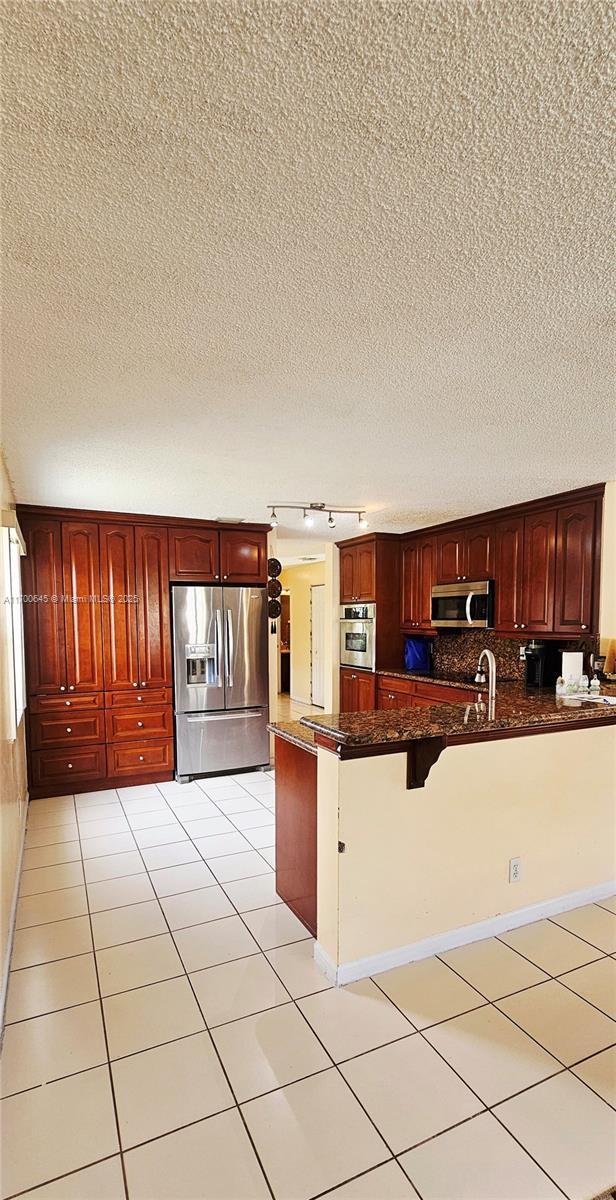 17352 SW 18th St, Miramar, FL 33029 - kitchen with appliances with stainless steel finishes, rail lighting, a textured ceiling, a peninsula, and light tile patterned flooring