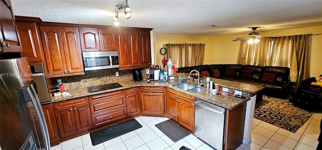 kitchen with kitchen peninsula, a textured ceiling, stainless steel appliances, sink, and dark stone countertops