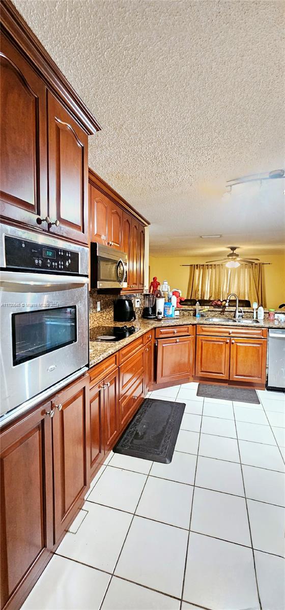 kitchen featuring backsplash, sink, a textured ceiling, light tile patterned flooring, and stainless steel appliances