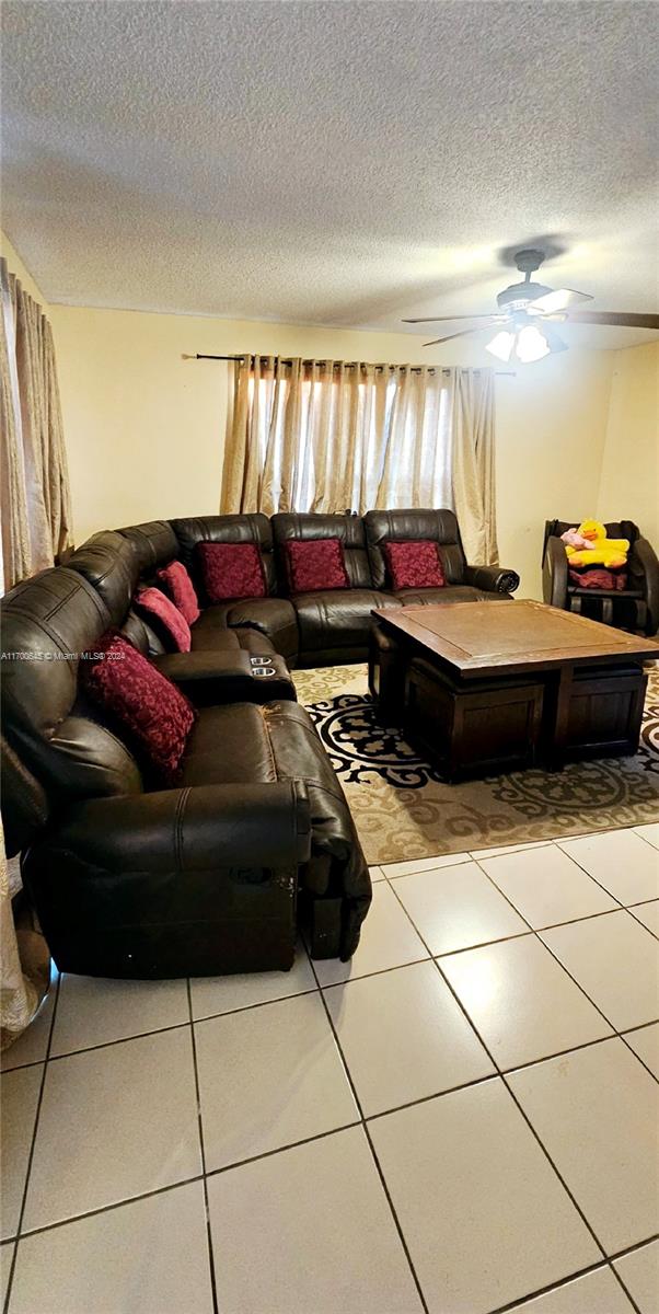 living room featuring tile patterned flooring, a textured ceiling, and ceiling fan