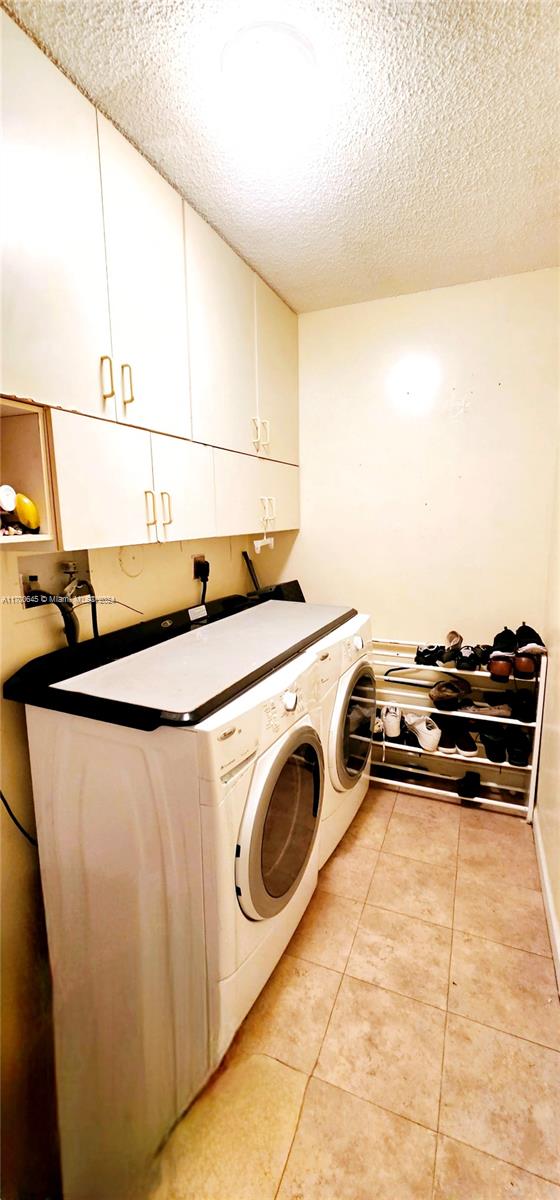 laundry room featuring cabinets, light tile patterned floors, a textured ceiling, and washer and dryer