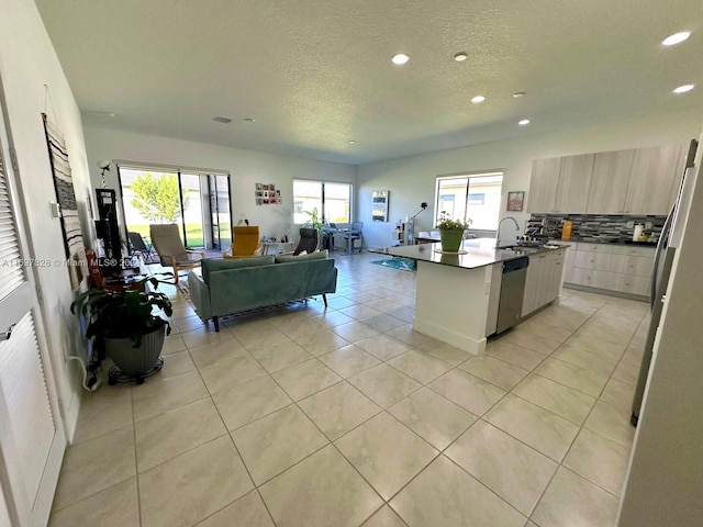 kitchen featuring dishwasher, a kitchen breakfast bar, decorative backsplash, an island with sink, and light tile patterned flooring