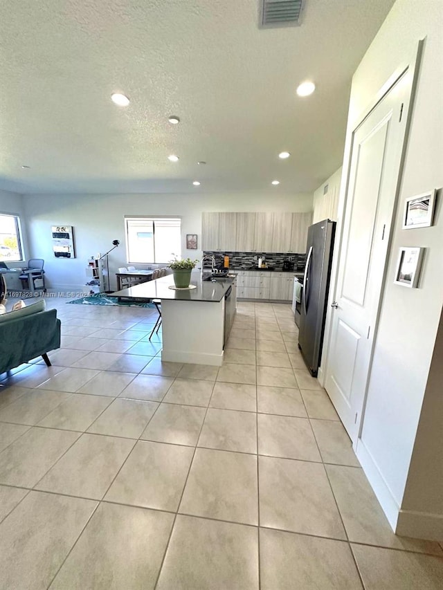 kitchen featuring a wealth of natural light, a kitchen breakfast bar, an island with sink, and stainless steel refrigerator