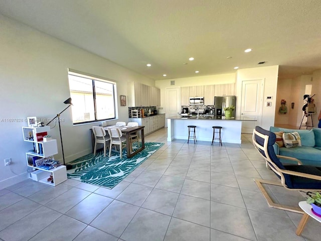 kitchen featuring a breakfast bar, light tile patterned floors, stainless steel appliances, and an island with sink