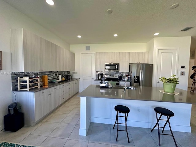 kitchen featuring light brown cabinets, an island with sink, appliances with stainless steel finishes, and tasteful backsplash