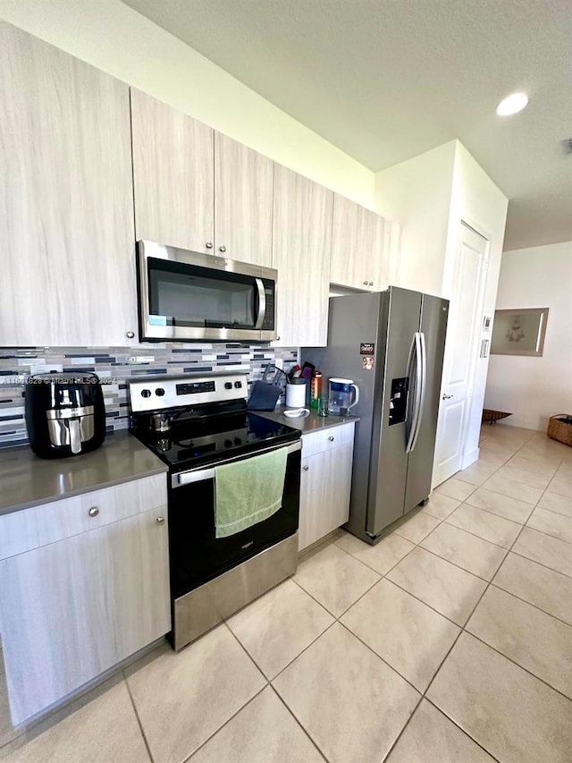 kitchen featuring backsplash, light brown cabinetry, light tile patterned floors, and appliances with stainless steel finishes