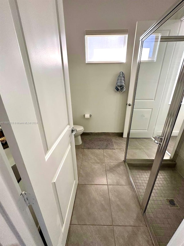 bathroom with tile patterned floors, toilet, and an enclosed shower