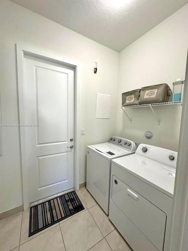 washroom with light tile patterned flooring, independent washer and dryer, and a textured ceiling