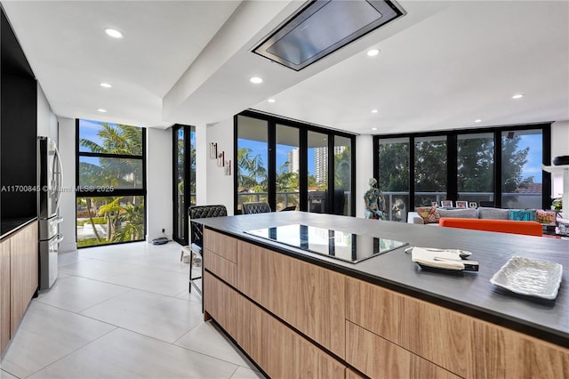 kitchen with expansive windows, black electric stovetop, light tile patterned flooring, and stainless steel refrigerator