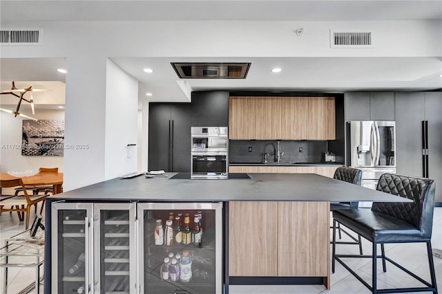 kitchen featuring a breakfast bar area, backsplash, stainless steel appliances, an island with sink, and beverage cooler