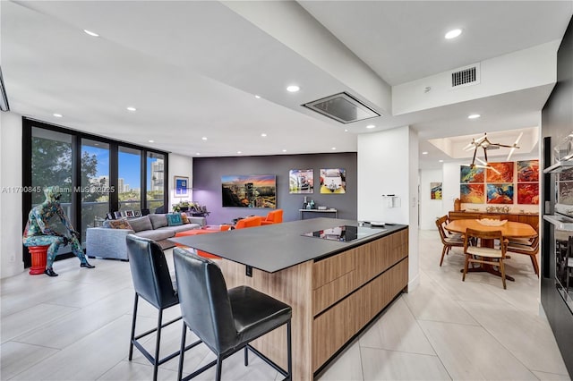 kitchen featuring a spacious island, a breakfast bar area, light tile patterned floors, a wall of windows, and black electric stovetop