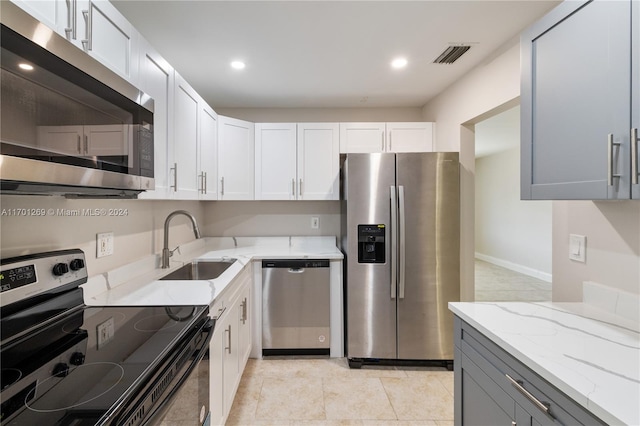 kitchen with gray cabinetry, white cabinetry, sink, light stone counters, and appliances with stainless steel finishes