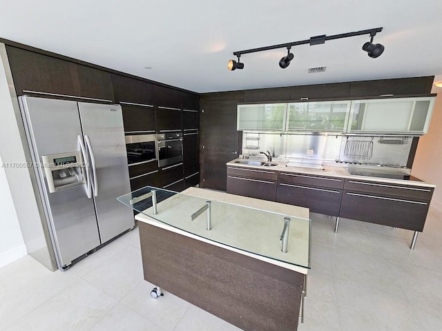 kitchen featuring track lighting, sink, appliances with stainless steel finishes, dark brown cabinets, and a kitchen island