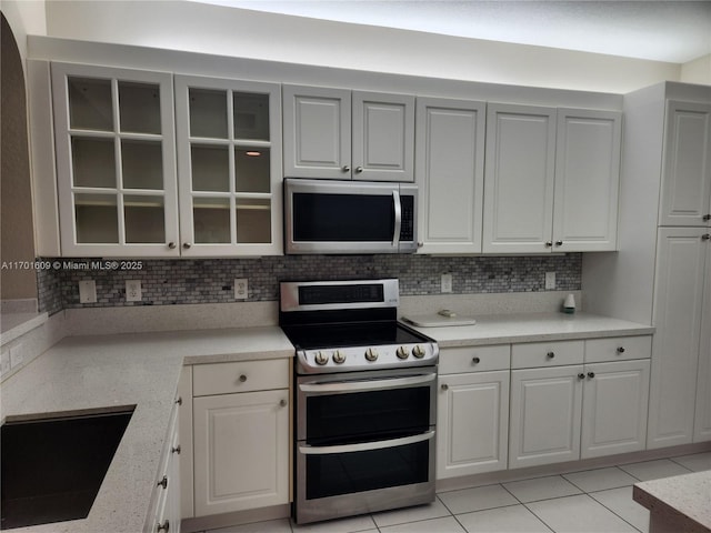 kitchen with white cabinetry, light tile patterned floors, decorative backsplash, sink, and stainless steel appliances