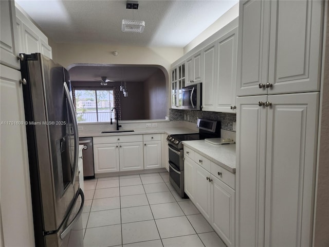 kitchen with a textured ceiling, appliances with stainless steel finishes, white cabinetry, sink, and light tile patterned flooring