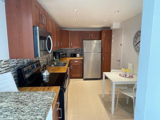 kitchen with appliances with stainless steel finishes, backsplash, light tile patterned floors, and sink