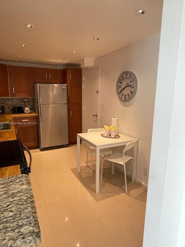 kitchen featuring stainless steel fridge, black stove, light tile patterned floors, and backsplash