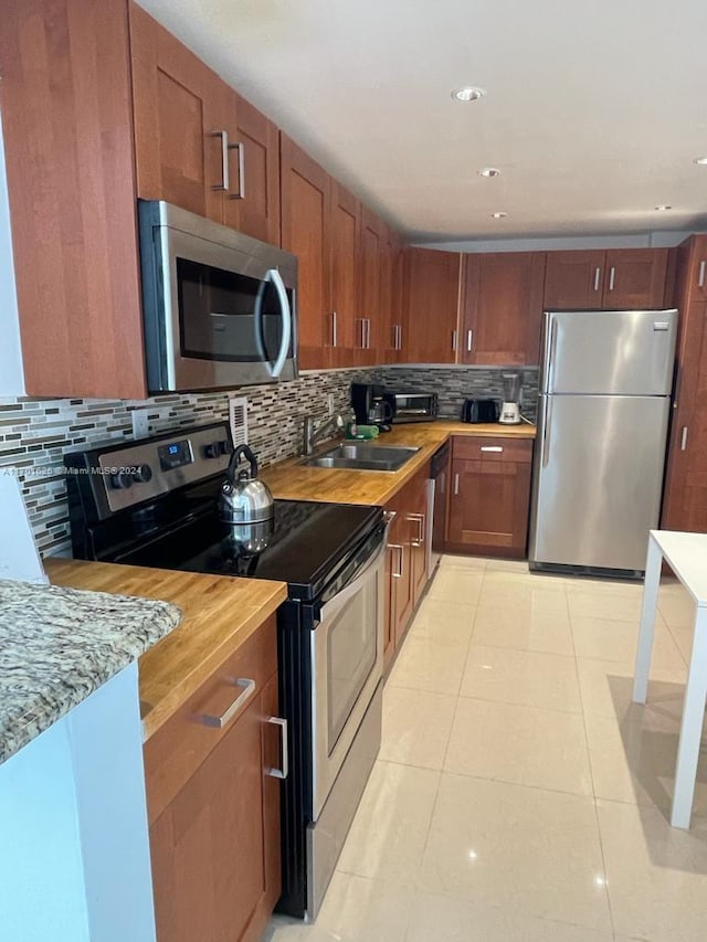 kitchen featuring sink, tasteful backsplash, light tile patterned flooring, butcher block counters, and stainless steel appliances