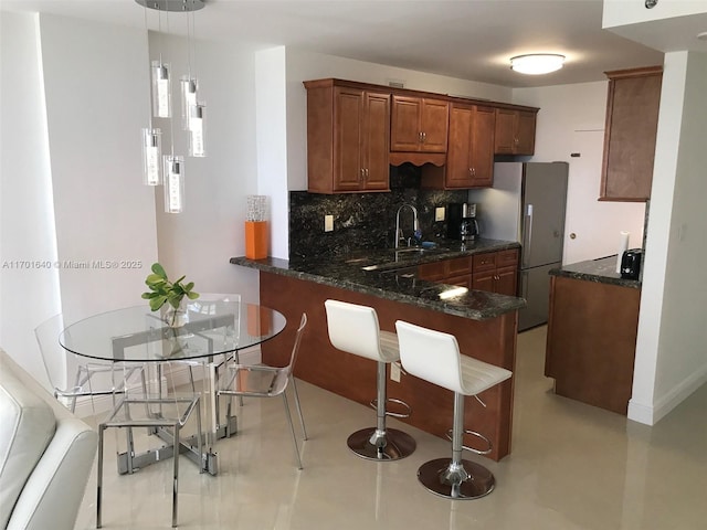 kitchen with kitchen peninsula, stainless steel fridge, backsplash, a kitchen breakfast bar, and hanging light fixtures