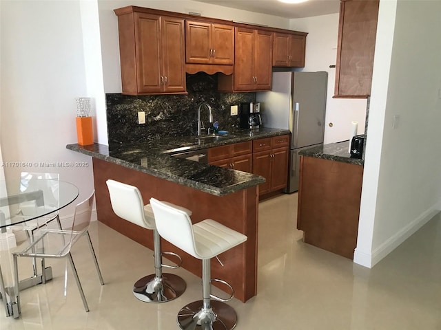 kitchen with kitchen peninsula, decorative backsplash, a kitchen bar, dark stone counters, and white refrigerator