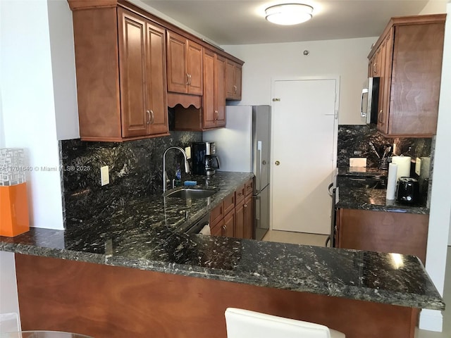 kitchen featuring sink, backsplash, kitchen peninsula, dark stone countertops, and appliances with stainless steel finishes