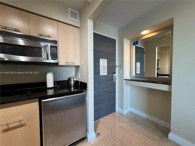 kitchen with light brown cabinets, visible vents, baseboards, stainless steel microwave, and dark stone countertops