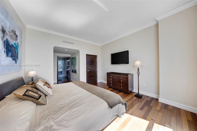 bedroom with ornamental molding, visible vents, baseboards, and wood finished floors