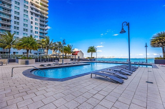 community pool with a patio, a water view, and fence