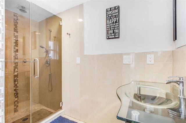 bathroom with a shower with door, tile walls, and sink