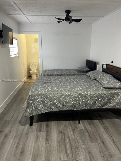 bedroom with hardwood / wood-style floors, ceiling fan, a drop ceiling, and connected bathroom