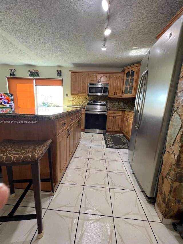 kitchen featuring backsplash, stainless steel appliances, a breakfast bar area, and a textured ceiling