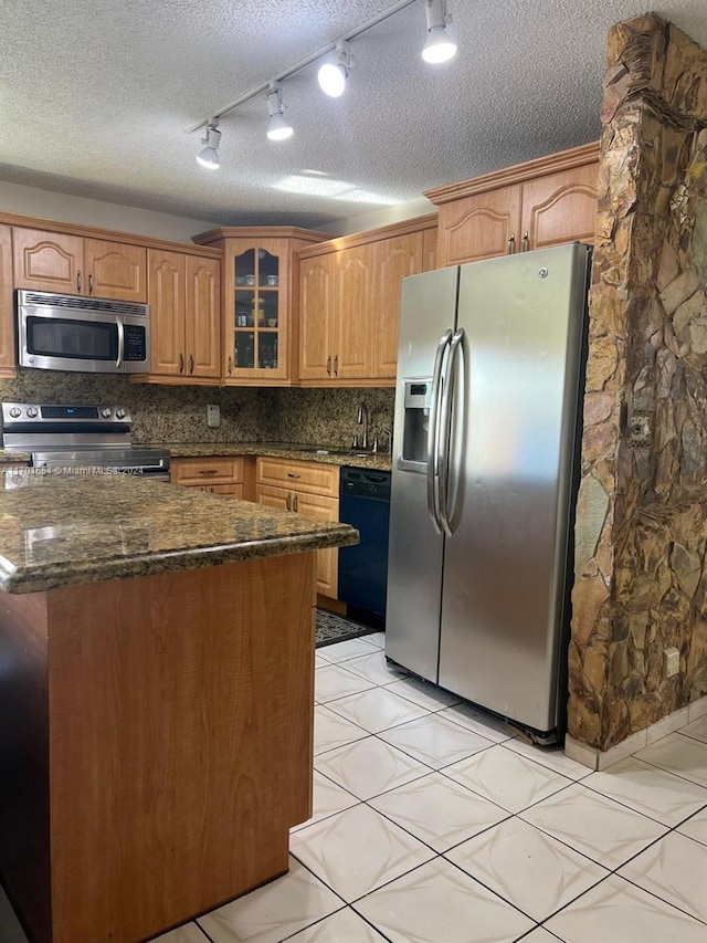 kitchen featuring sink, stainless steel appliances, dark stone countertops, a textured ceiling, and decorative backsplash