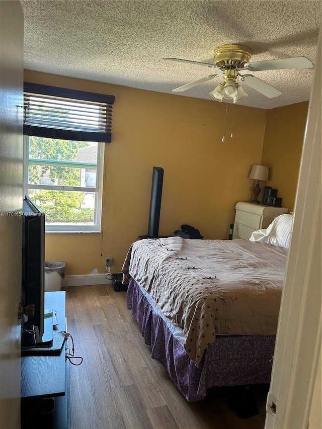 bedroom with hardwood / wood-style floors, ceiling fan, and a textured ceiling