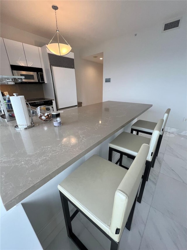 kitchen with white cabinetry, light stone countertops, hanging light fixtures, kitchen peninsula, and a breakfast bar