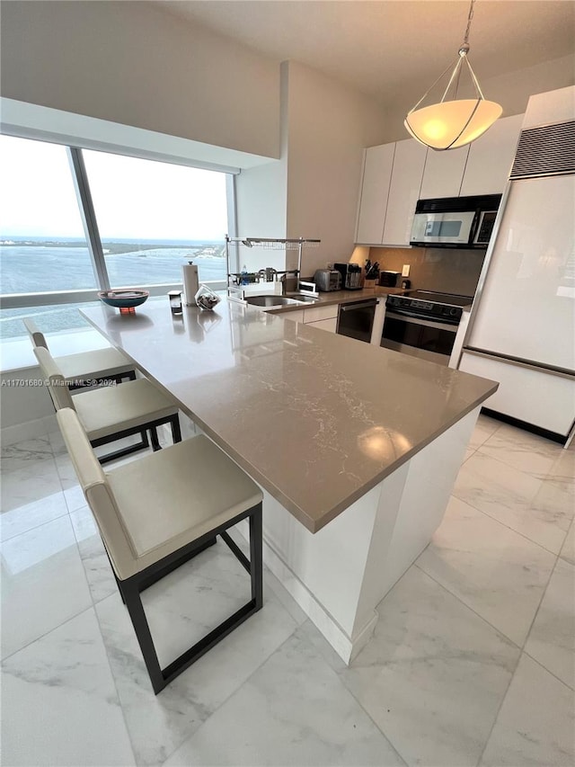 kitchen with appliances with stainless steel finishes, a water view, white cabinets, hanging light fixtures, and a breakfast bar area