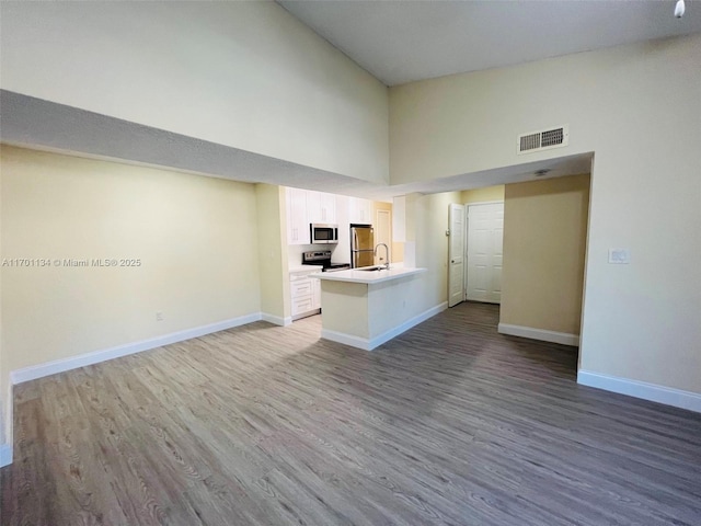 unfurnished living room featuring hardwood / wood-style flooring, high vaulted ceiling, and sink