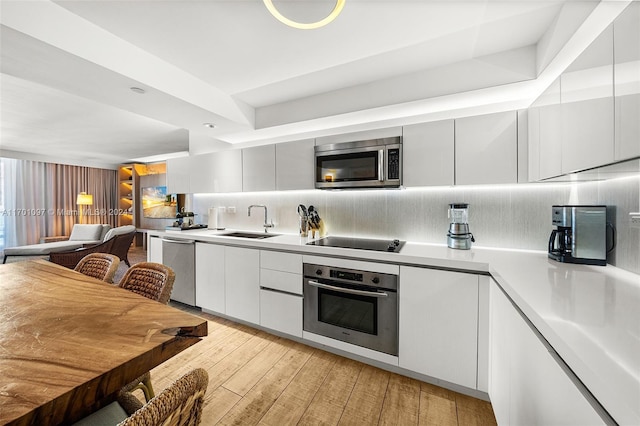 kitchen with white cabinets, sink, tasteful backsplash, light hardwood / wood-style floors, and stainless steel appliances