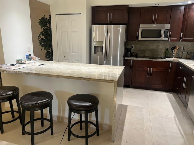 kitchen with light stone countertops, stainless steel appliances, tasteful backsplash, and a breakfast bar area