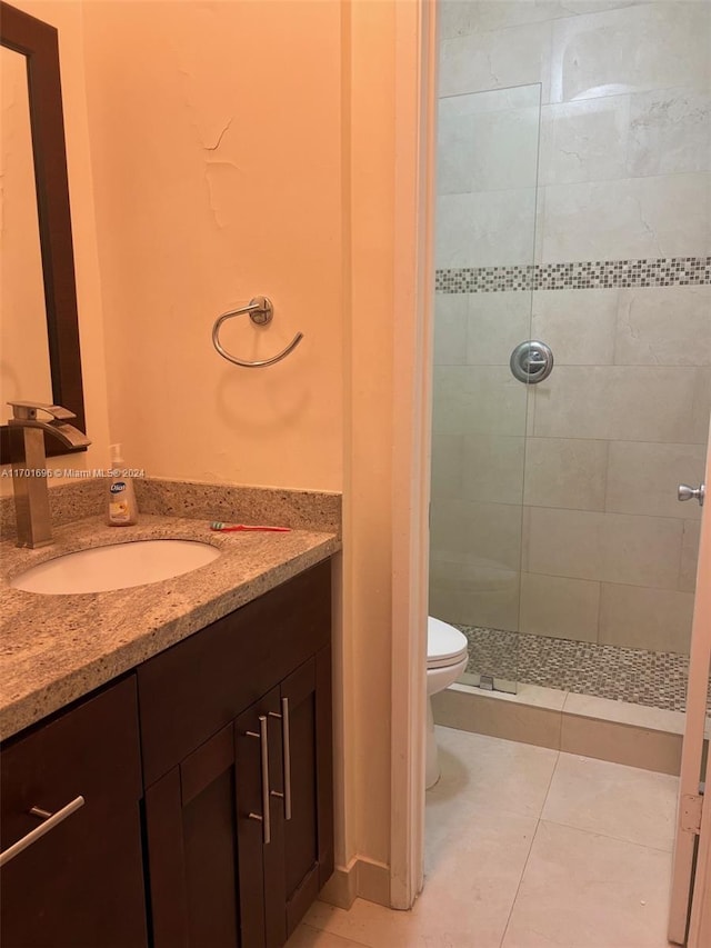 bathroom with a tile shower, tile patterned flooring, vanity, and toilet