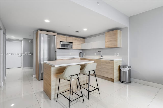 kitchen with light tile patterned flooring, sink, appliances with stainless steel finishes, a kitchen island, and a breakfast bar area