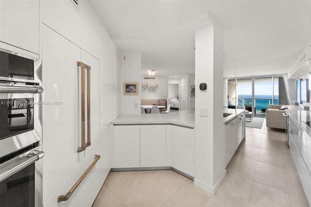 kitchen with floor to ceiling windows, white cabinetry, oven, and light tile patterned floors