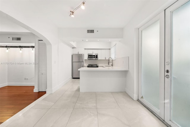 kitchen with white cabinetry, sink, kitchen peninsula, appliances with stainless steel finishes, and light wood-type flooring