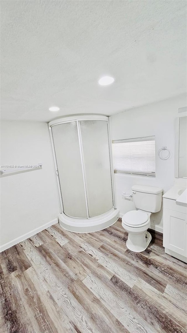 bathroom with hardwood / wood-style flooring, vanity, toilet, and a shower with door